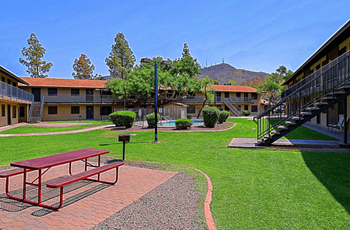 A red picnic table is in the middle of a grassy courtyard with view of the pool in the background at Sahuaro West, Phoenix 85029
